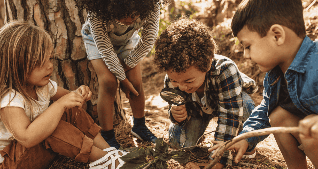 Stock (1500 x 800 px) (4) four kids looking at a leaf through a magnifying glass.